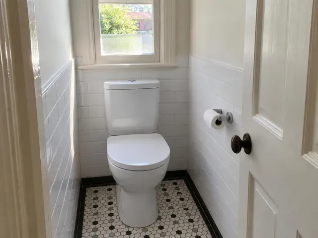 Clean white toilet in a narrow tiled bathroom with a window and patterned floor in Vaucluse