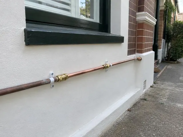 Copper water pipe fixed along an exterior rendered wall beside a window in Double Bay