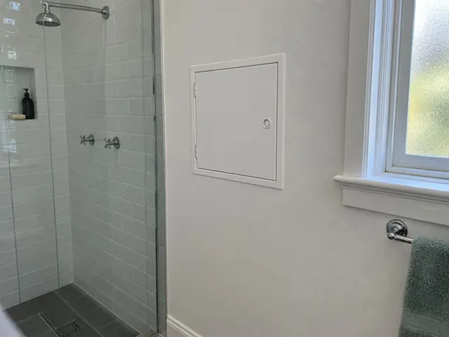 Small access panel on a painted bathroom wall beside a tiled shower and window in Vaucluse